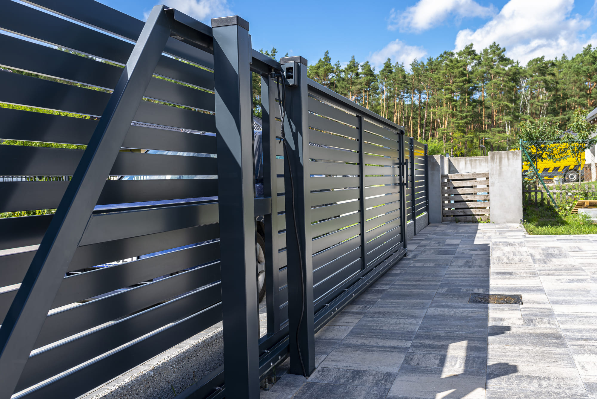 Modern panel fencing sliding metal fence and gate with a paved driveway and lush garden in view